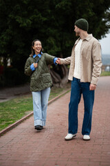 Obraz premium Happy diverse couple walking holding hands in park