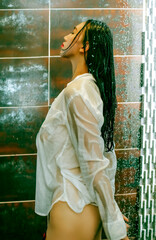 An Asian woman wearing a white shirt is taking a shower in the bathroom.