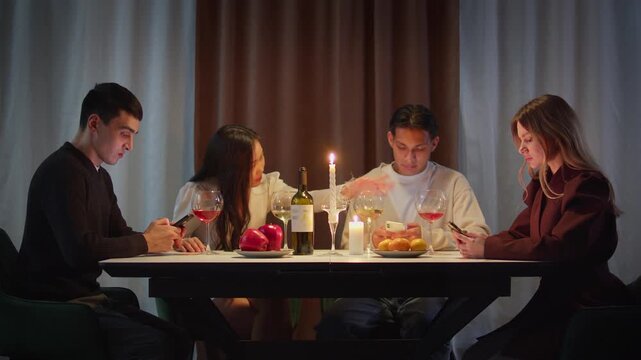 Group friends with cell mobile phone addiction having evening wine dinner together. People celebrating event. Awkward ignore double date problem at restaurant or home. Holiday candle light atmosphere.