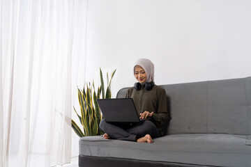 Woman with headscarf smiling on video call with headphones and laptop, engaged remote meeting and virtual collaboration scene,
