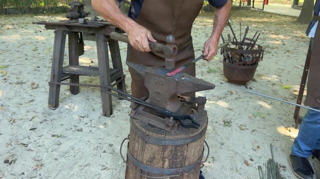 Blacksmith hammers glowing hot iron on anvil, close up