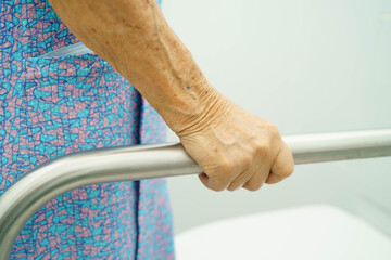 Asian elderly woman patient use toilet support rail in bathroom.