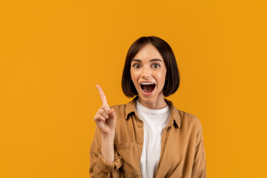 Wow, eureka. Emotional woman having great idea, finding inspiration or solution to problem, posing with open mouth over yellow background. Amazed lady pointing finger up
