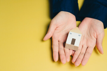 New house concept. Person holds small wooden house model their hands, symbolizing home ownership and real estate investment. bright yellow background adds cheerful