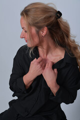 Fototapeta premium Elegante Frau im schwarzen Outfit sitzend auf Hocker vor hellem Studiohintergrund. Zeitlose Portraitfotografie mit natürlicher Pose und klarer Ästhetik. Ideal für Business, Lifestyle, Mode, Editorial 