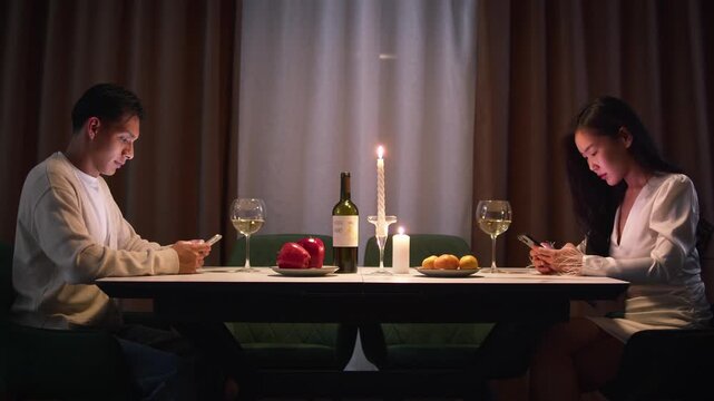Couple with cell mobile phone addiction having evening wine dinner together. People celebrating event. Awkward ignore romantic first date problem at restaurant or home. Holiday candle light atmosphere