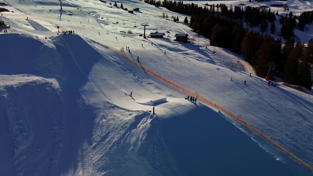 Aerial view of the Seiser Alm snowpark. Freestyle ski jumps with the Seiser Alm logo are seen against the backdrop of vast snow-covered plateaus and distant mountain peaks. Alpe di Siusi, Italy