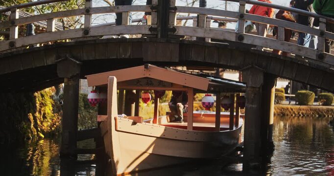 Beautiful, old, wooden Japanese boat floating under village bridge at sunset