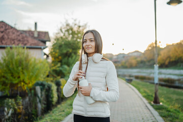 Fototapeta premium Woman walking on a path, holding a water bottle and wearing headphones