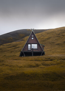 View of a solitary A-frame cabin standing proudly amidst a field of golden grass under a brooding sky, a quiet retreat, Torshavn, Faroe Islands.