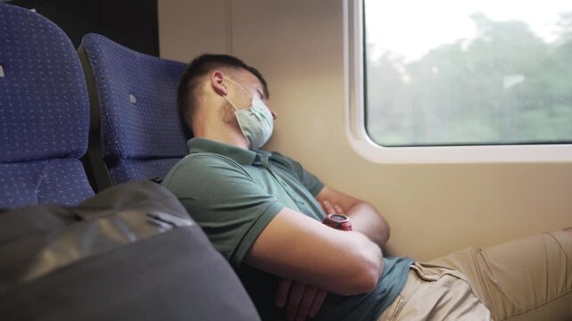 Travel safely public transport. Young man in medical mask sleeps near train window. Train passenger in protective mask on face resting. New normal travel concept. Commuter sleep covid 19, coronavirus.