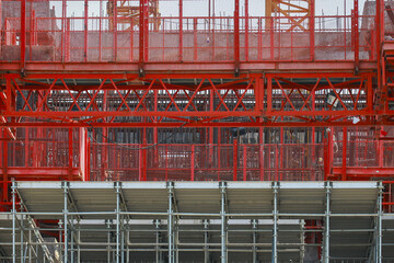 Vibrant red metal scaffolding structure stands prominently against construction site backdrop, showcasing intricate patterns and industrial design. scene captures essence of urban development