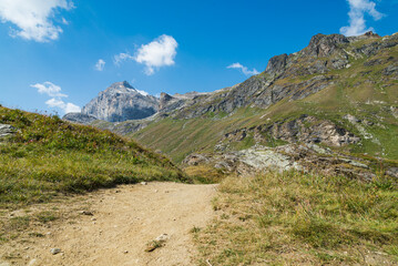 Dirt road of the hiking track leading to the mountain named "Granta Parey", Rhemes Valley, Aosta Valley, Italy. Blue sky and white clouds on the background.