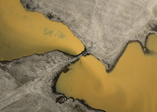 Aerial view of land meeting the water, creating a stark contrast between the earthy tones and the golden hues of the water, Selfoss, Iceland.