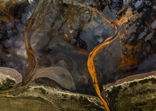 Aerial view of winding, vibrant orange rivers cutting through a stark landscape of grey and brown earth, sculpting intricate patterns from above, Selfoss, Sveitarfelagid Arborg, Iceland.