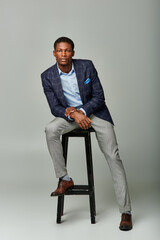 Confident young man strikes a stylish pose while seated on a high stool in a modern studio