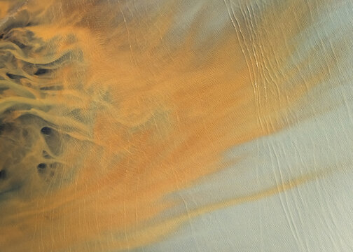 Aerial view of contrasting orange sediment plumes swirling into the pale blue waters, creating an abstract natural artwork, Selfoss, Sveitarfelagid Arborg, Iceland.