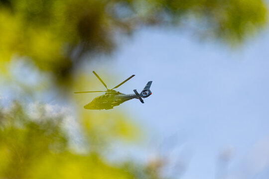 Helic&oacute;ptero sobrevoando entre folhas de &aacute;rvore em um c&eacute;u azul. 