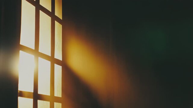 Warm golden sun rays stream through a large window onto a dark interior wall, casting light and shadow that evoke hope, calm, and the promise of new beginnings