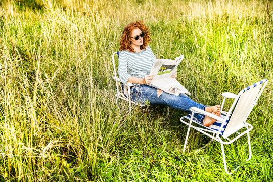 Young woman relaxing on a meadow reading newspaper