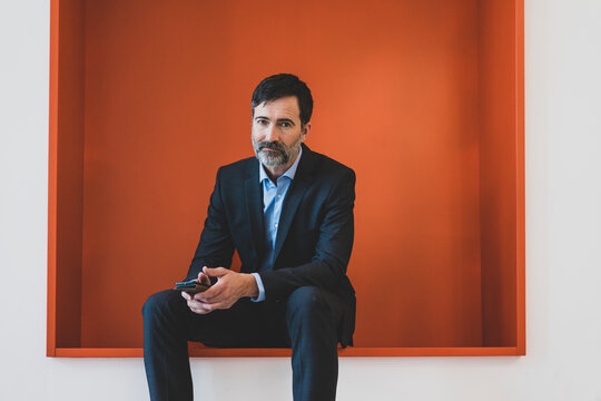 Mature businessman sitting in a niche holding cell phone