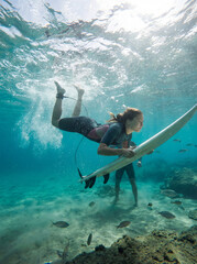 A young female surfer learns to surf in shallow water. She dives underwater with her surfboard.