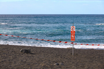 Restricted Beach Access at Playa Jard&iacute;n, Puerto de la Cruz &mdash; Red Warning Sign and Barrier Tape Against Ocean Waves on Volcanic Sand
