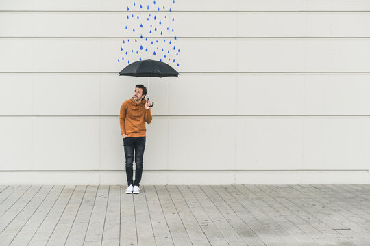 Digital composite of young man holding an umbrella at a wall with raindrops