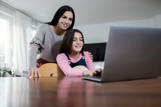 Mother and daughter smiling in front of laptop with daughter holding a guitar