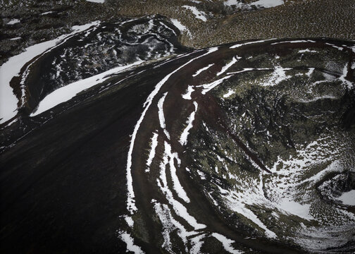 Aerial view of stark black volcanic earth slashed with brilliant white snow, creating an otherworldly landscape of fire and ice, Flugir, Rangarthing ytra, Iceland.