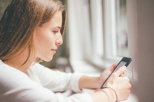 Young woman holding portable device at the window