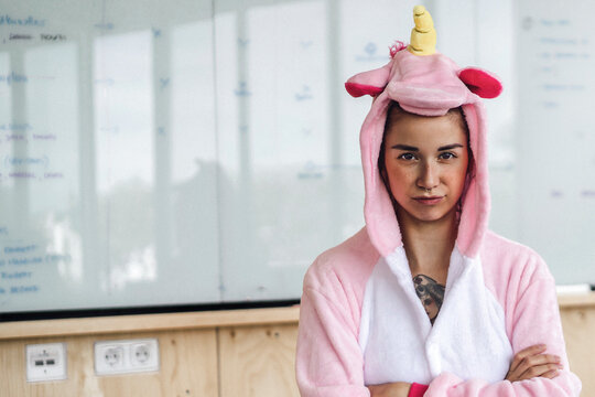 Woman wearing unicorn onesie, standing in front of whiteboard, looking stubborn