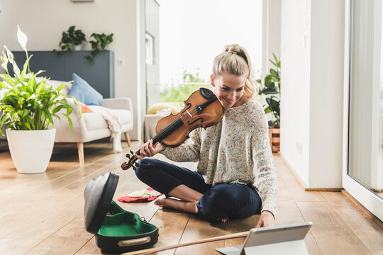 Woman with tablet sitting on the floor at home playing violin