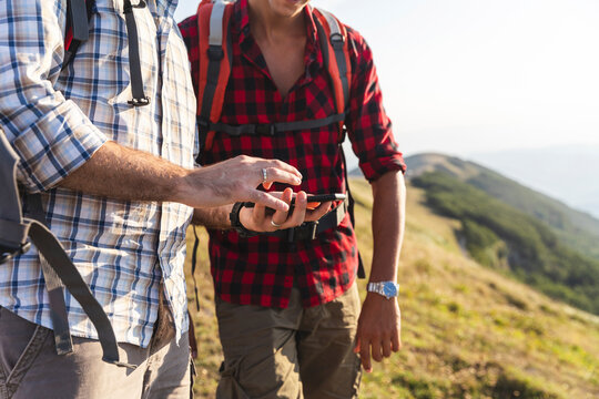 Italy, Monte Nerone, close-up of two men hiking and using smartphone in mountains