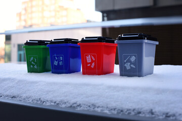 Colorful recycling toy boxes standing in snow, plastic classification trash cans as children's...