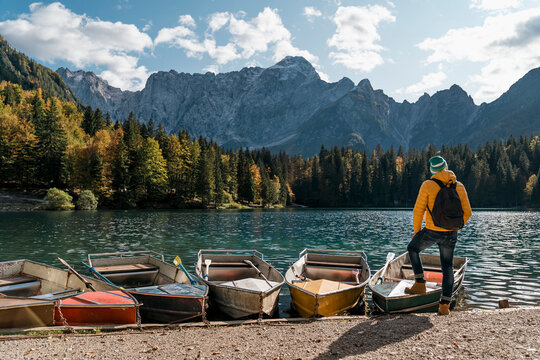 Hiker standing at mooring area with boats at Laghi di Fusine, Friuli Venezia Giulia, Italy