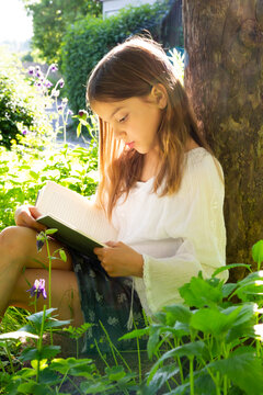 Little girl leaning against tree trunk reading a book