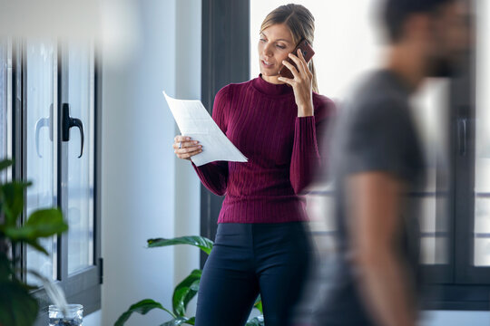 Businesswoman talking over smart phone while male coworker walking in office
