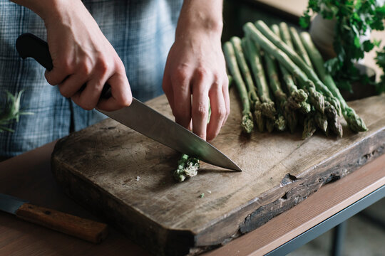 Hands of man cutting fresh asparagus on board in kitchen