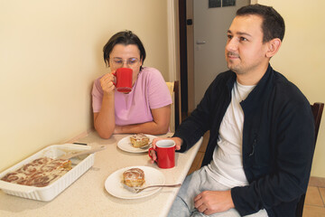 Young caucasian couple enjoying coffee and cinnamon rolls in kitchen
