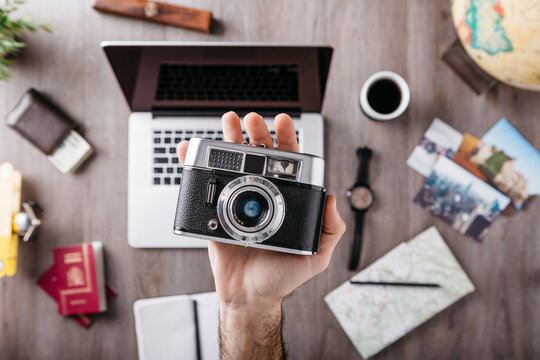 Overhead view of man's hand holding camera and travel items on table