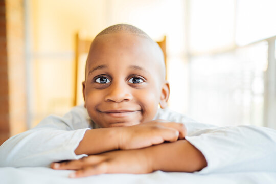 Close-up of smiling boy with shaved head leaning on table at home
