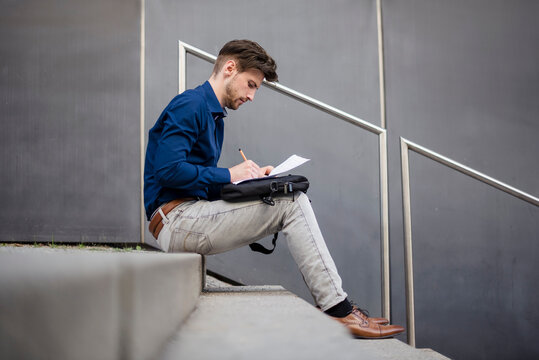 Businessman sitting on stairs outdoors taking notes