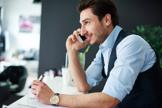 Smiling hairdresser talking on cell phone at the counter