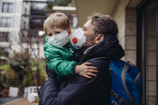 Father carrying son, both wearing protective maska, outdoors