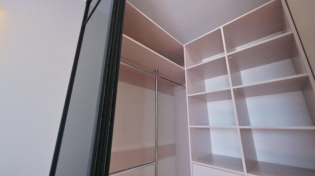 A modern built-in wardrobe with sliding glass doors, open shelving, hanging rails, and closed compartments &mdash; sleek design in neutral tones, ideal for efficient storage.
