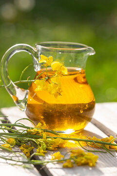 Rapeseed oil in jar with rape blossom on wood