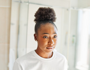 Fototapeta premium Portrait of a young beautiful black woman in front of mirror in bathroom in morning, skin care, beauty and hygiene concepts