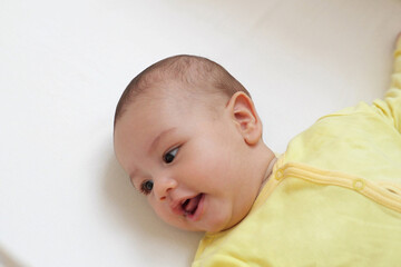 A nice little caucasian newborn baby is funny smiling, lying at child bed. Beautiful Smiling Baby on the bed at home
