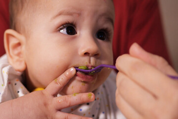 Portrait of little baby boy eating food. Baby with a spoon in feeding chair. Cute baby eating first meal